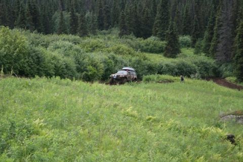 1990 Chevrolet Suburban - A muddy, lifted Chevrolet Suburban is stuck in the mud in a grassy field with a dense forest in the background. A person stands in the fiel…