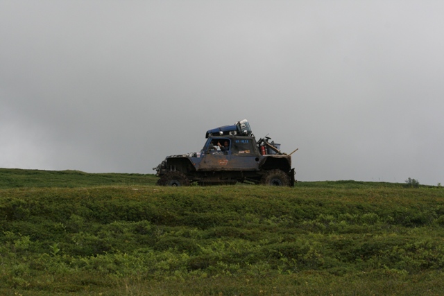 Truck driving across a grassy field under a cloudy sky