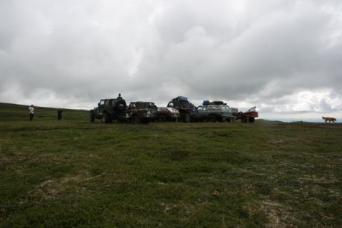 1990 Chevrolet Suburban - A group of off-road vehicles are gathered in a wide, grassy landscape under an overcast sky.