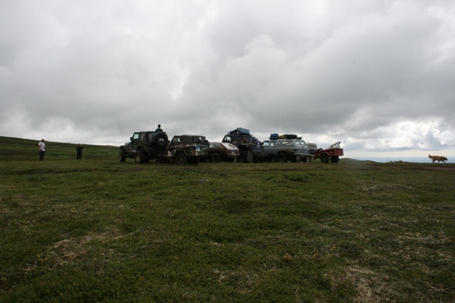 Several off-road vehicles parked on a grassy hill under a cloudy sky
