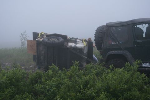 1990 Chevrolet Suburban - A dark green Jeep Wrangler is parked next to an overturned trailer in a foggy, grassy field. A person is visible in the trailer, appearing…