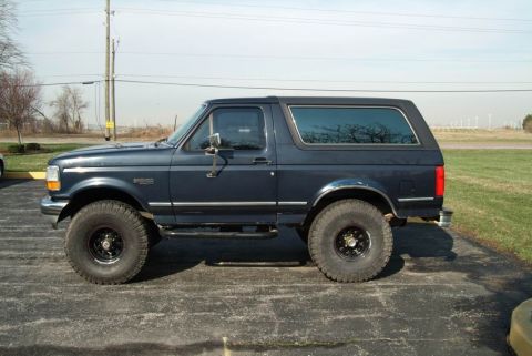 1992 Ford Bronco - A dark blue 1992 Ford Bronco SUV is shown from the side, parked outdoors.