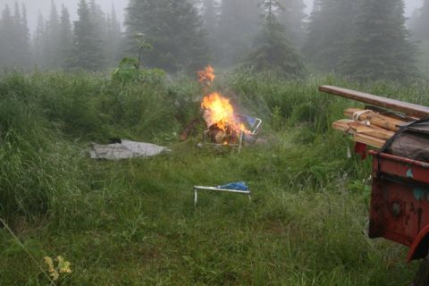 1990 Chevrolet Suburban - A campfire burns in a grassy field with a trailer and lumber in the foreground.