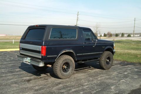 1992 Ford Bronco - The rear quarter panel of a dark blue Ford Bronco is visible, with a silver stripe and tinted windows.