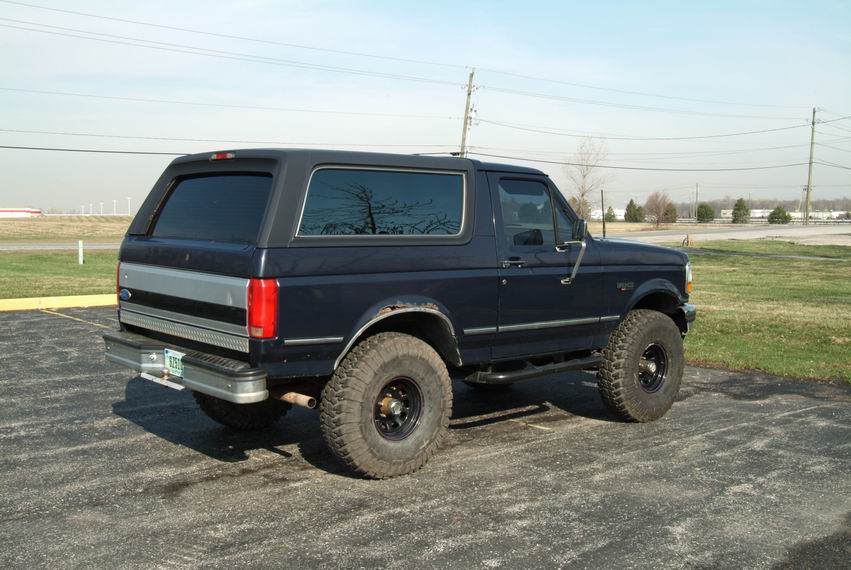 Dark blue Ford Bronco parked on asphalt, side view showing lifted suspension and off-road tires