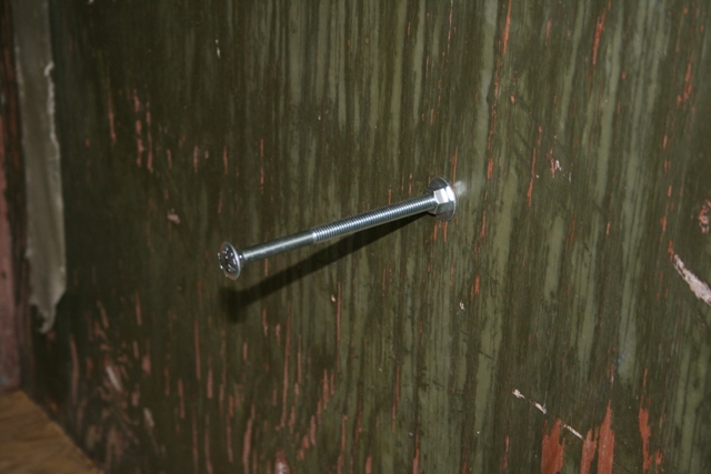 Long bolt with a nut and washer going through a green, weathered wall