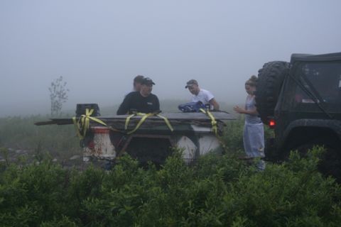 1990 Chevrolet Suburban - People load lumber onto a trailer in foggy weather, with a dark SUV nearby.