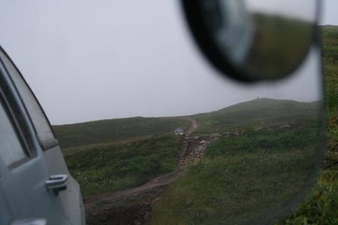1990 Chevrolet Suburban - Two vehicles navigate a challenging dirt track on a misty, green hillside.