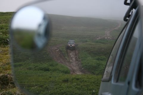 1990 Chevrolet Suburban - An off-road vehicle navigates a dirt track in a misty, green terrain.