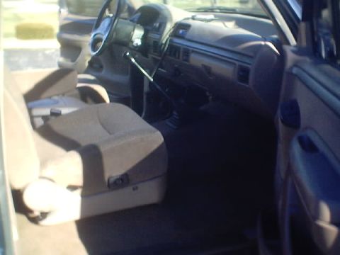 1992 Ford Bronco - The interior of a truck shows the driver's seat, dashboard, and steering wheel, with a view of the exterior through the windows.