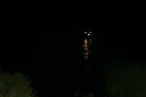 1990 Chevrolet Suburban - A dark scene at night shows a vehicle with its taillights illuminated, partially submerged in water. The reflection of the taillights can b…