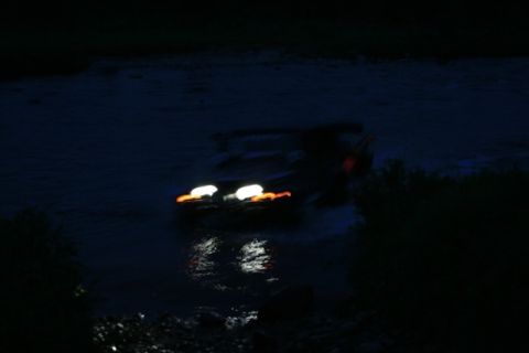 1990 Chevrolet Suburban - A dark, blurry image shows a vehicle with its headlights on, driving through water at night. The water reflects the vehicle's lights.