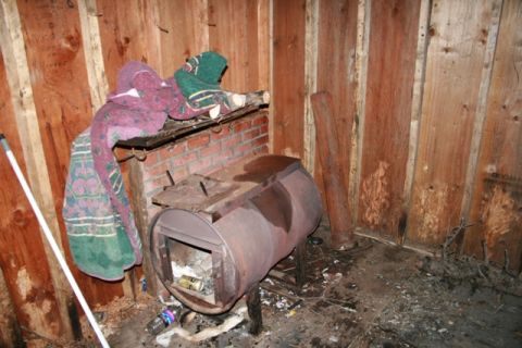 1990 Chevrolet Suburban - The interior of a rustic structure with wooden walls, a makeshift metal stove, and blankets draped over a shelf.