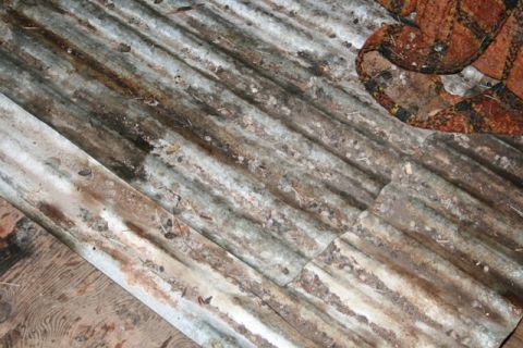 1990 Chevrolet Suburban - A close-up view of weathered corrugated metal roofing with debris scattered on its surface. A portion of a patterned fabric is visible in t…