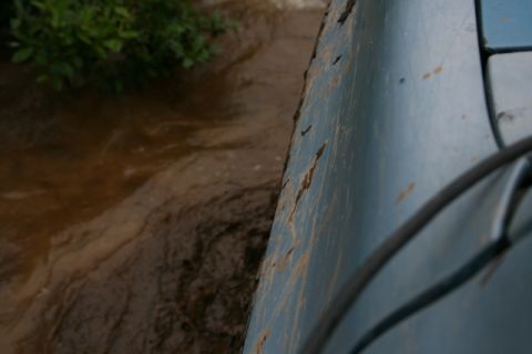 1990 Chevrolet Suburban - A close-up, low-angle shot shows the side of a light blue vehicle, possibly a Chevrolet Suburban, with mud splatters and some rust or damag…