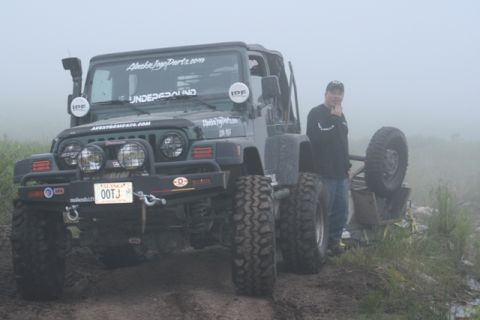 1990 Chevrolet Suburban - A modified green Jeep Wrangler is parked on a muddy trail in foggy conditions. A man stands next to the Jeep, looking towards the camera.