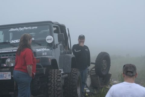 1990 Chevrolet Suburban - A dark green Jeep Wrangler is parked in a foggy outdoor setting. A woman in a red shirt and jeans stands to the left of the Jeep, and a man…