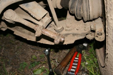 1990 Chevrolet Suburban - A close-up view of the underside of a vehicle's suspension system, showing a tie rod end and other components. Tools including a wrench, ha…