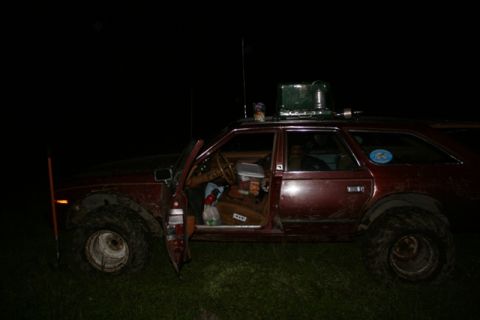 1990 Chevrolet Suburban - A maroon station wagon with oversized tires and a portable stove mounted on the roof is parked in a grassy area at night. The driver's side…
