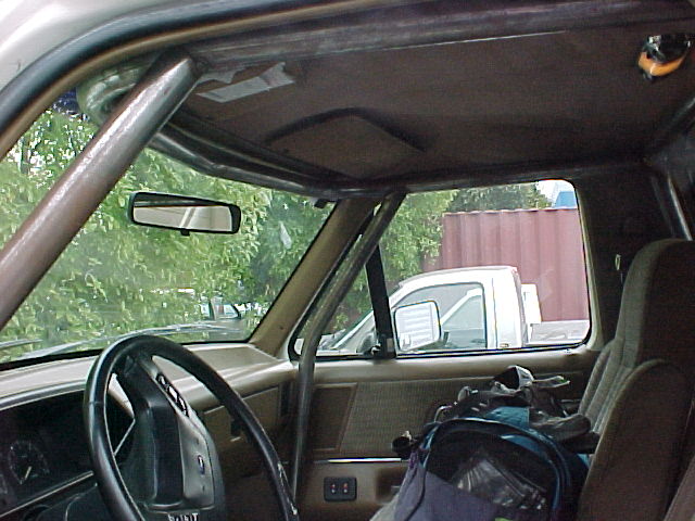 Truck interior with roll bar, rearview mirror and view of white truck outside
