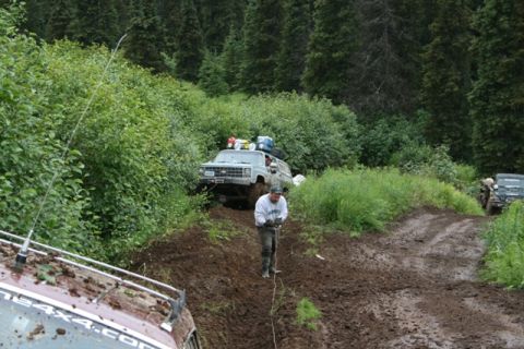 1990 Chevrolet Suburban - A light blue Chevrolet Suburban is stuck in the mud on a steep, wooded trail. A man is standing in front of the vehicle, holding a rope tha…