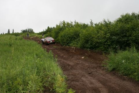 1990 Chevrolet Suburban - A brown and white SUV is stuck in the mud on a dirt track, with two people standing nearby. The vehicle is on an incline surrounded by tall…