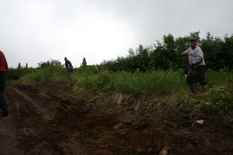 1990 Chevrolet Suburban - Two men are working on a muddy incline with dense green foliage and trees in the background under an overcast sky.