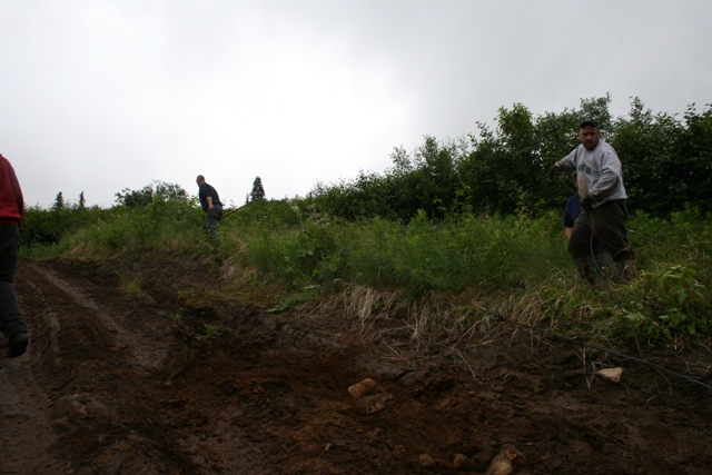 Two men on a muddy hill with trees and foliage.