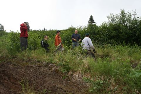 1990 Chevrolet Suburban - A group of five men stand in a grassy, wooded area next to a muddy embankment. One man in a red hoodie is on the far left, and the others a…
