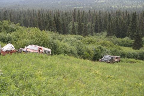1990 Chevrolet Suburban - Two off-road vehicles are parked in a grassy field with a dense forest in the background. A red and white pickup truck with a camper shell…