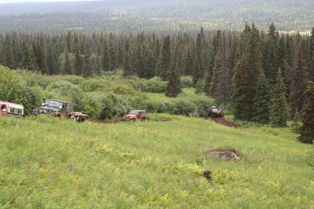 Several off-road vehicles driving on a muddy trail in a forest.