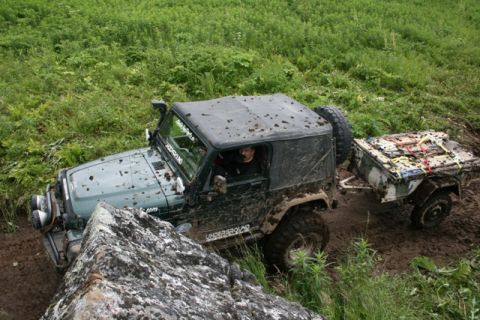 1990 Chevrolet Suburban - A green Jeep Wrangler is navigating a muddy, off-road trail with a trailer attached. The vehicle is covered in mud and is partially obscure…