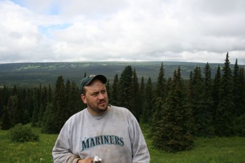 1990 Chevrolet Suburban - A man wearing a grey sweatshirt with "MARINERS" written on it and a green baseball cap stands in a grassy field with a dense forest and clo…