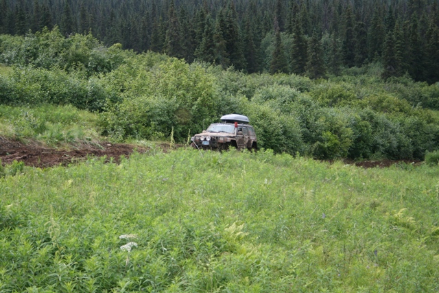 Brown SUV with roof carrier on a muddy track in a forest.