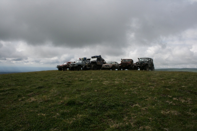 Six off-road vehicles lined up on a grassy hill under a cloudy sky.