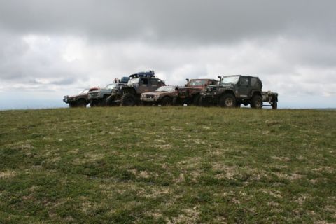 1990 Chevrolet Suburban - A line of modified off-road vehicles are parked on a grassy hilltop under a cloudy sky. The vehicles include several Jeeps and SUVs with la…