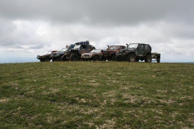 Several modified off-road SUVs and Jeeps parked in a line on a grassy hill.