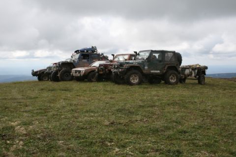 1990 Chevrolet Suburban - A line of modified off-road vehicles, including several Jeeps and a blue truck, are parked on a grassy hilltop under a cloudy sky.