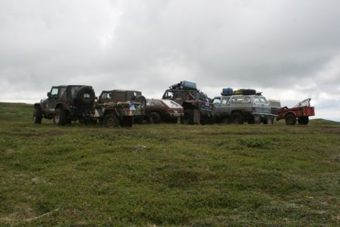 1990 Chevrolet Suburban - A line of off-road vehicles, including a Jeep and a Chevrolet Suburban, are parked on a grassy, overcast hillside.