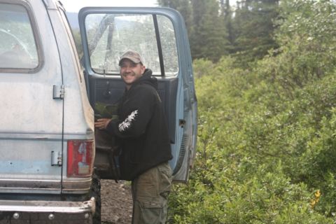 1990 Chevrolet Suburban - A man wearing a baseball cap and a black hoodie smiles as he stands next to the open driver's side door of a light blue Chevrolet Suburban.