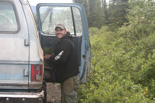 Man smiling next to the open door of a light blue Chevrolet Suburban.