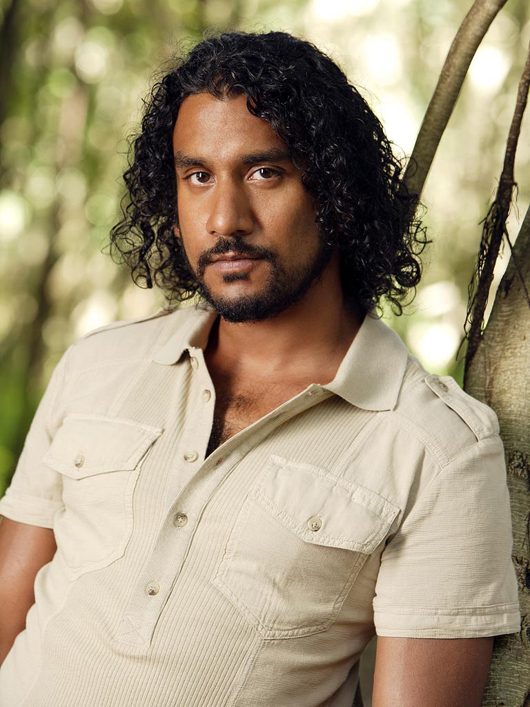 Man with curly hair leaning against a tree