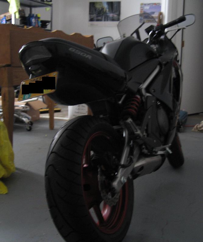 Black 650R sportbike from the rear in a garage with red wheels and shock spring