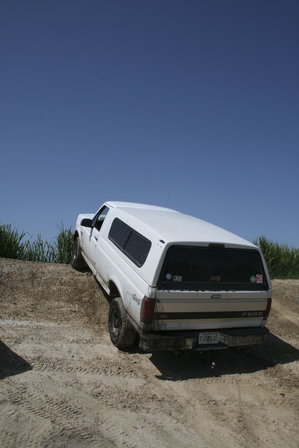 White Ford pickup with camper shell parked nose-down on a dirt mound