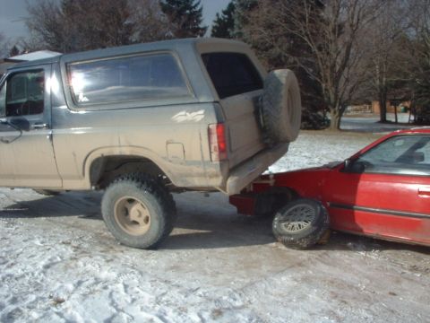 1986 Ford Bronco - A Ford Bronco has collided with a red car, with the Bronco's front end resting on the car's hood.