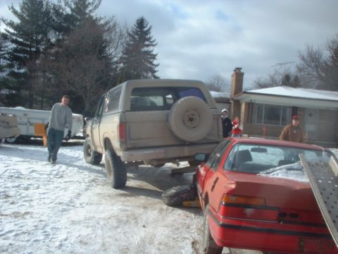 1986 Ford Bronco - A tan Ford Bronco is parked in the snow, with a red car in the foreground.
