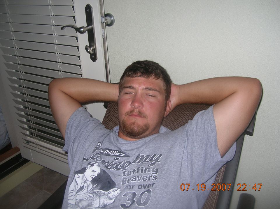Man relaxing with hands behind head, eyes closed, wearing a grey t-shirt.