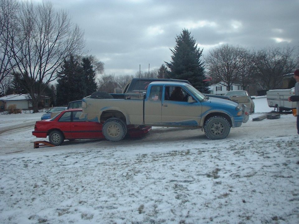 Pickup truck on top of a red car in a snowy lot