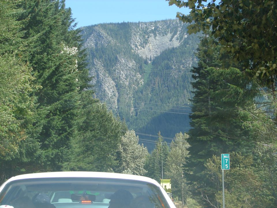 Rear view of a white sedan driving past a mountain and a mile marker sign.