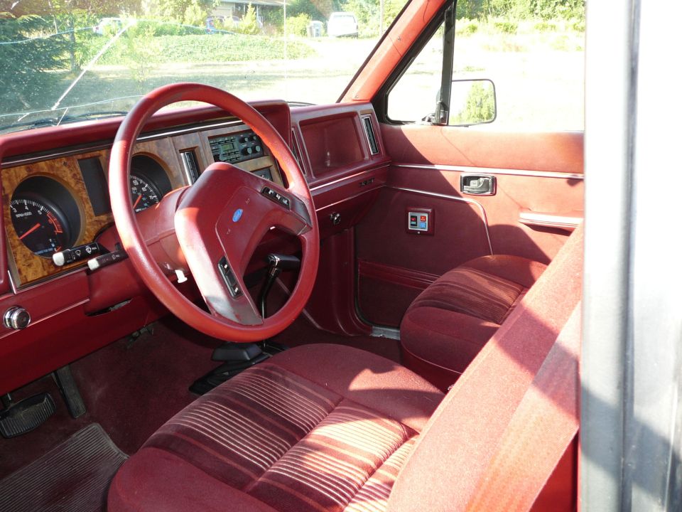 All-red interior of a Ford Bronco II with red steering wheel, woodgrain dash trim, and striped cloth seats